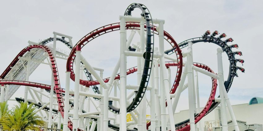 A thrilling red roller coaster with multiple loops under a clear sky, offering an exhilarating ride.