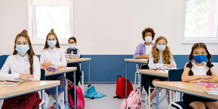 Students in masks seated at desks in a classroom, maintaining safety measures.