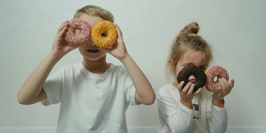 Two children having fun with colorful doughnuts as eyeglasses indoors.